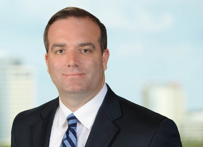Man in a suit and striped tie poses for a professional headshot with a blurred cityscape background.