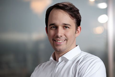 Dark haired man in a white shirt smiles in front of a soft blurred background