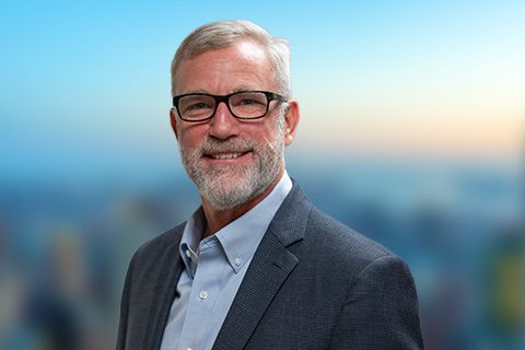 Bearded man in glasses and a blazer appears on a bright blurred background