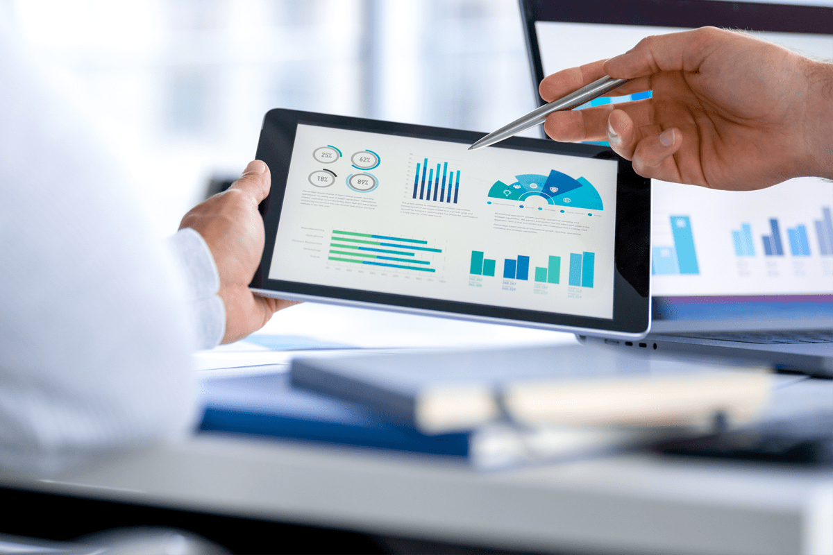 Two people review a tablet displaying various charts and graphs, with a laptop showing similar data in the background.