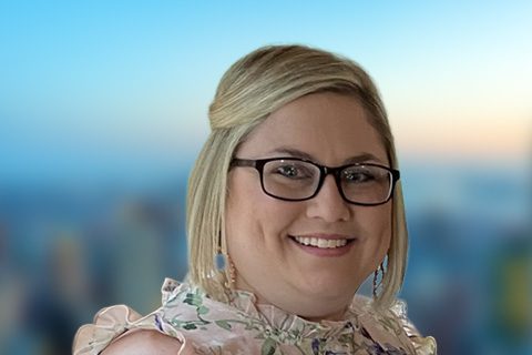 Blonde woman in glasses smiles in front of a bright blurred background