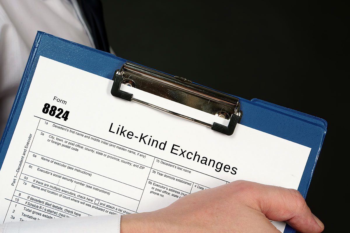 A person holds a clipboard with IRS Form 8824 titled Like-Kind Exchanges visible on top.