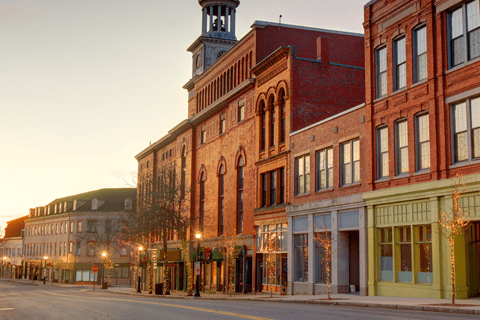 A quiet, empty street lined with historic brick buildings at sunrise, featuring a prominent clock tower in the center background.
