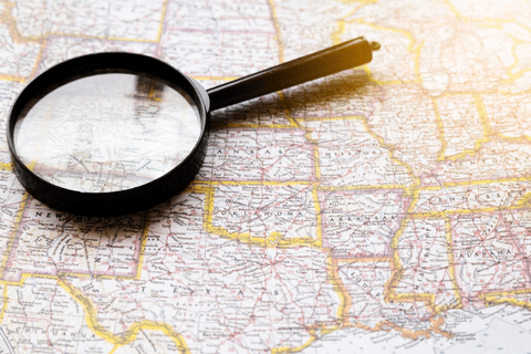 A magnifying glass rests on a map of the central United States, highlighting state borders and city names.