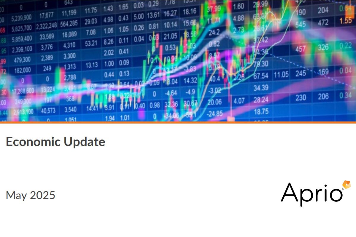 A digital screen displays stock market graphs and data above a report cover titled Economic Update, May 2025, with the Aprio logo.