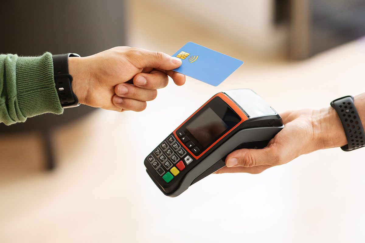A person holds a contactless credit card near a payment terminal held by another person, preparing to make a transaction.