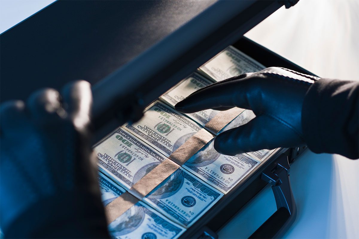 A person wearing black gloves opens a briefcase filled with stacks of U.S. hundred-dollar bills.