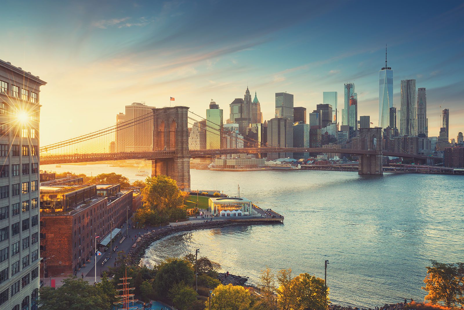 The Brooklyn Bridge spans the East River with the Manhattan skyline in the background at sunset in New York City.