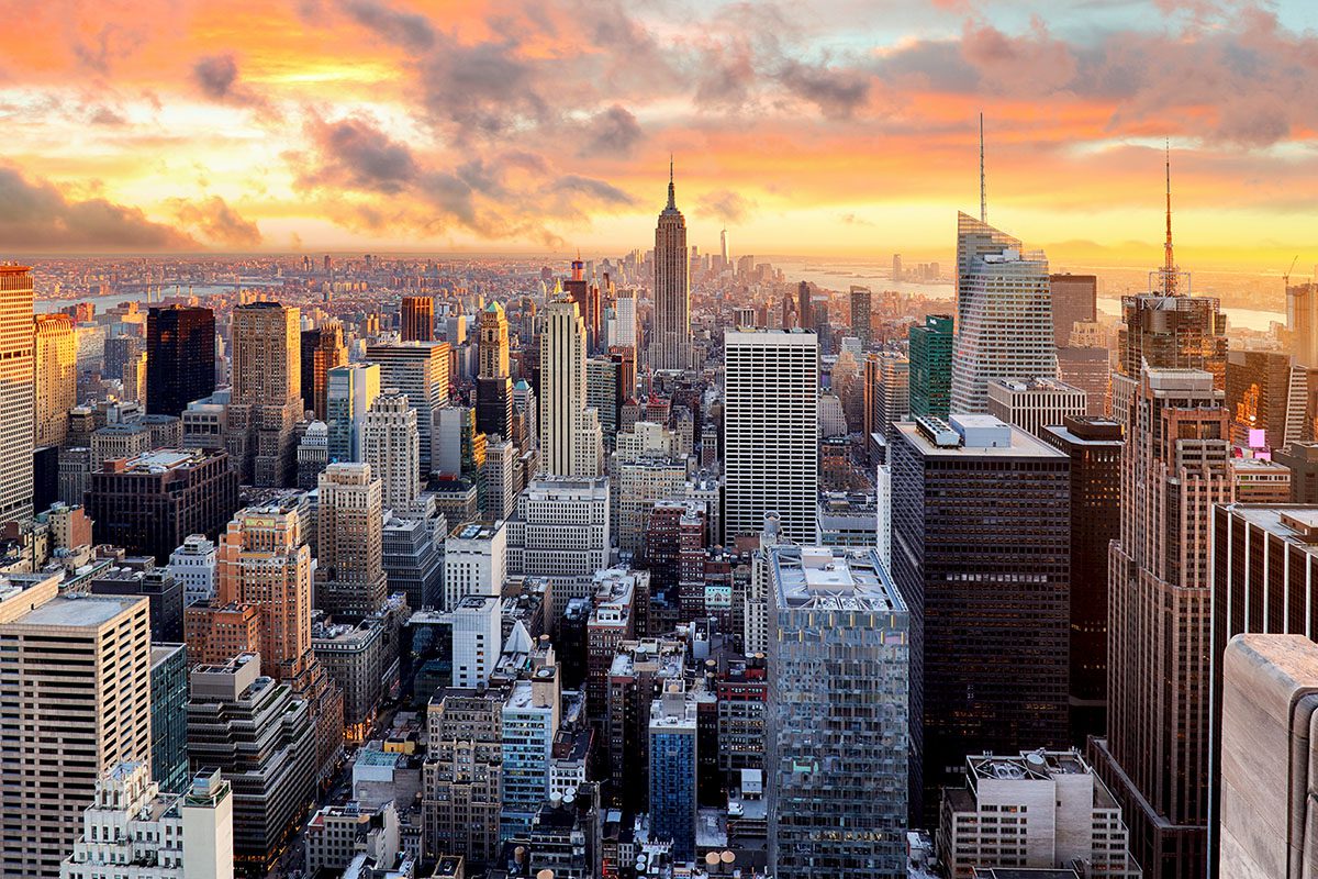 Aerial view of New York City skyscrapers at sunset, with the Empire State Building in the center and a partly cloudy sky above.