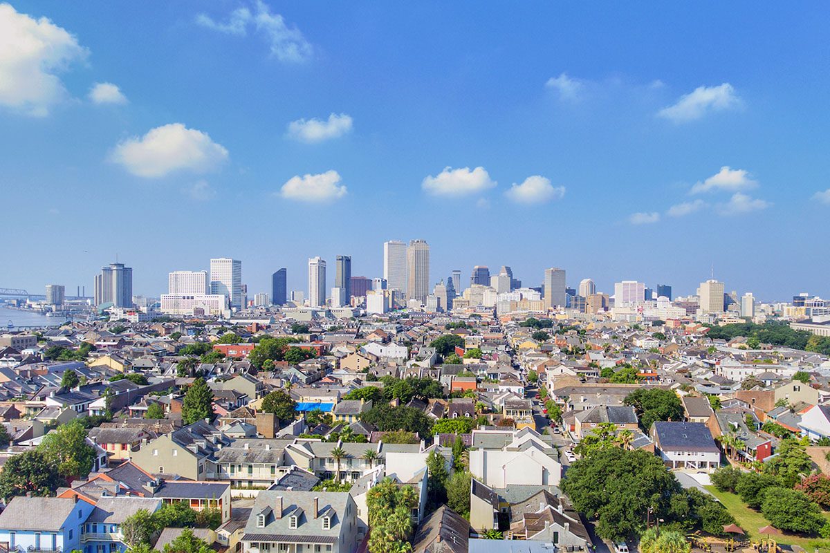 Aerial view of a residential neighborhood in the foreground with a city skyline of tall buildings in the background under a clear blue sky.