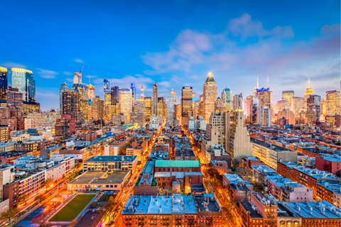 Aerial view of Midtown Manhattan, New York City, at sunset with illuminated skyscrapers and city streets.