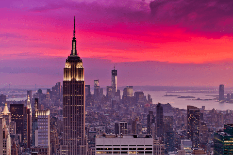 The Empire State Building and New York City skyline are shown at dusk, with a vivid pink and purple sunset in the background.