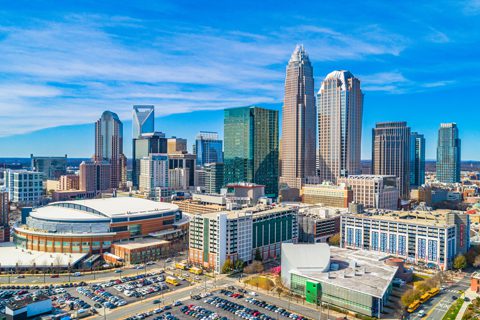 Aerial view of a modern city skyline with tall skyscrapers, a sports arena, and surrounding buildings under a blue sky.