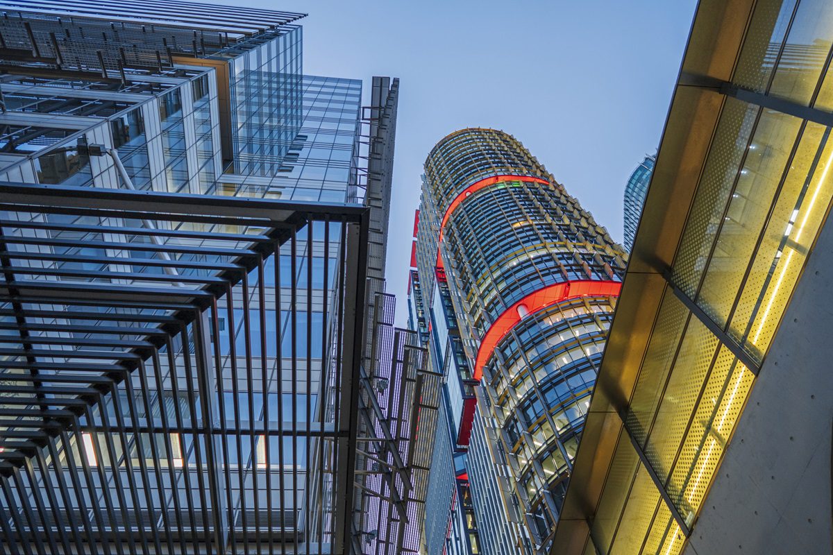 View looking up at modern high-rise office buildings with glass facades and metal structures against a clear blue sky.