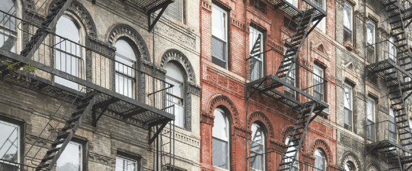 Rows of old apartment buildings with brick facades and black metal fire escapes on each floor.