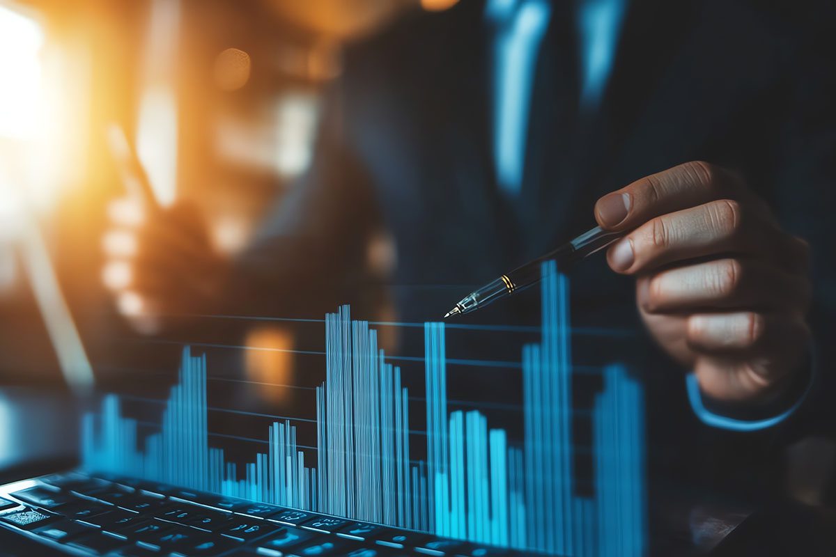 A person in a suit points at a digital bar graph displayed above a keyboard, suggesting data analysis or financial review.