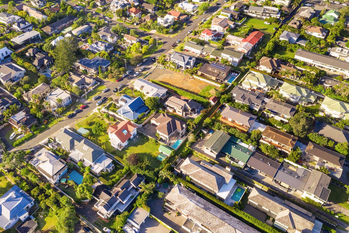 Aerial view of a suburban neighborhood with houses, green lawns, trees, and intersecting roads under daylight.