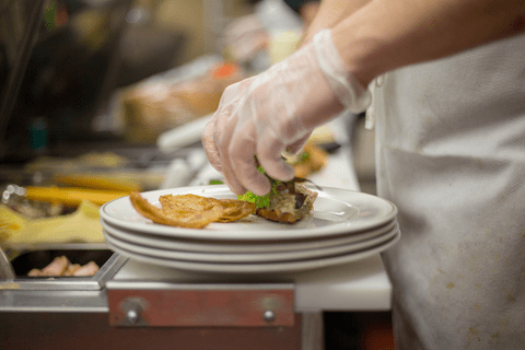 A person wearing gloves arranges food on stacked plates in a kitchen setting.