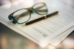 A pair of eyeglasses and a pen rest on top of a printed resume document on a desk.