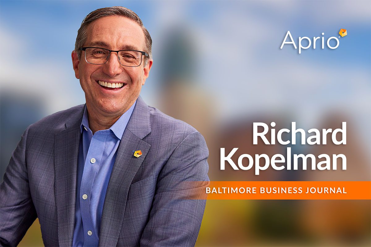 A man in a suit and glasses smiles in front of a blurred background with text: Aprio, Richard Kopelman, Baltimore Business Journal.