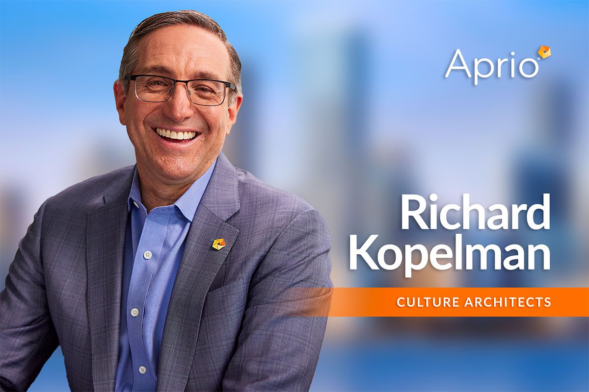 Smiling man in a suit poses in front of a blurred cityscape background with the text Aprio, Richard Kopelman, Culture Architects.
