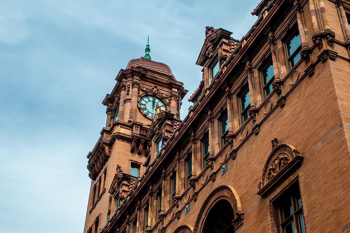A brick building with a clock tower and arched windows stands against a blue sky.
