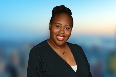 Dark haired woman in a black top smiles in front of a bright window with a blurred city view