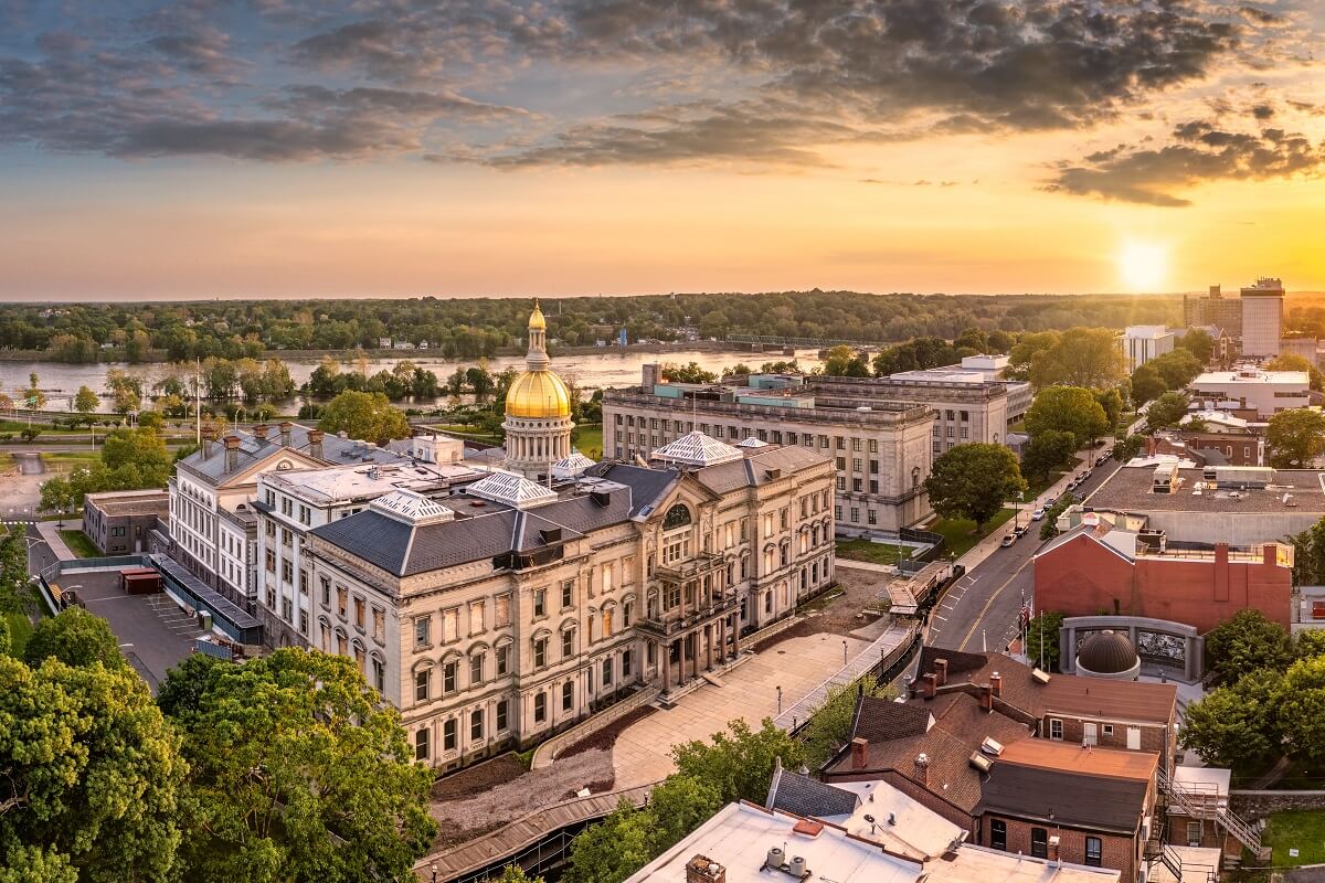 Aerial view of a historic government building with a gold dome at sunset, surrounded by trees, roads, and nearby buildings.