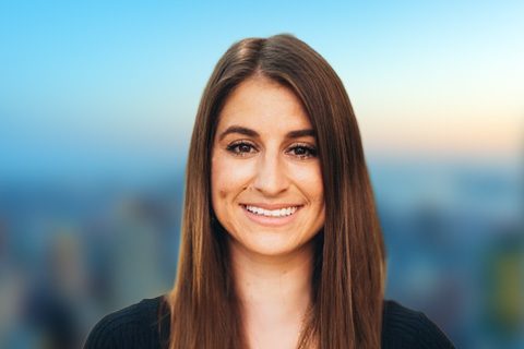 Dark haired woman smiles in front of a bright window with a blurred city view