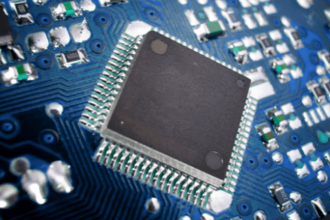 Close-up view of a microchip mounted on a blue printed circuit board with various electronic components and traces visible.