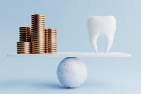 Stacks of coins and a large tooth are balanced on opposite sides of a white board resting on a round marble sphere against a light blue background.