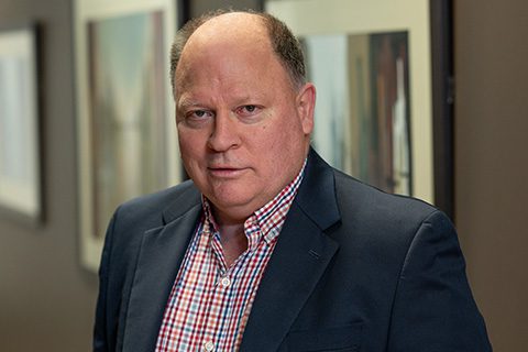 Man in a blazer stands in a hallway with paintings hanging on the walls