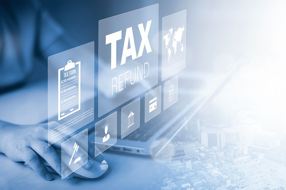 A person uses a laptop with virtual icons floating above it, including the words TAX REFUND and various financial symbols.