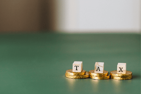Stacks of gold coins with wooden letter blocks spelling TAX on a green surface.