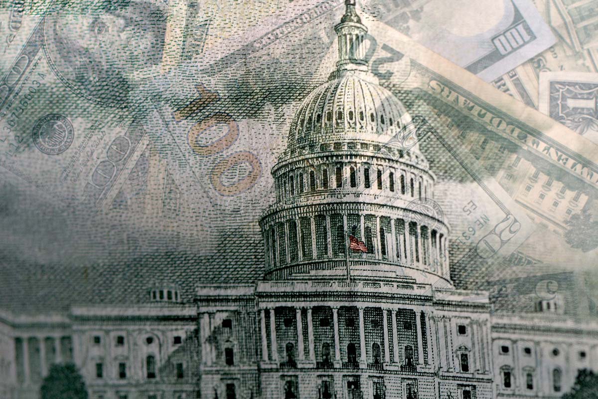 A close-up of the U.S. Capitol building overlaid with various denominations of U.S. dollar bills in the background.