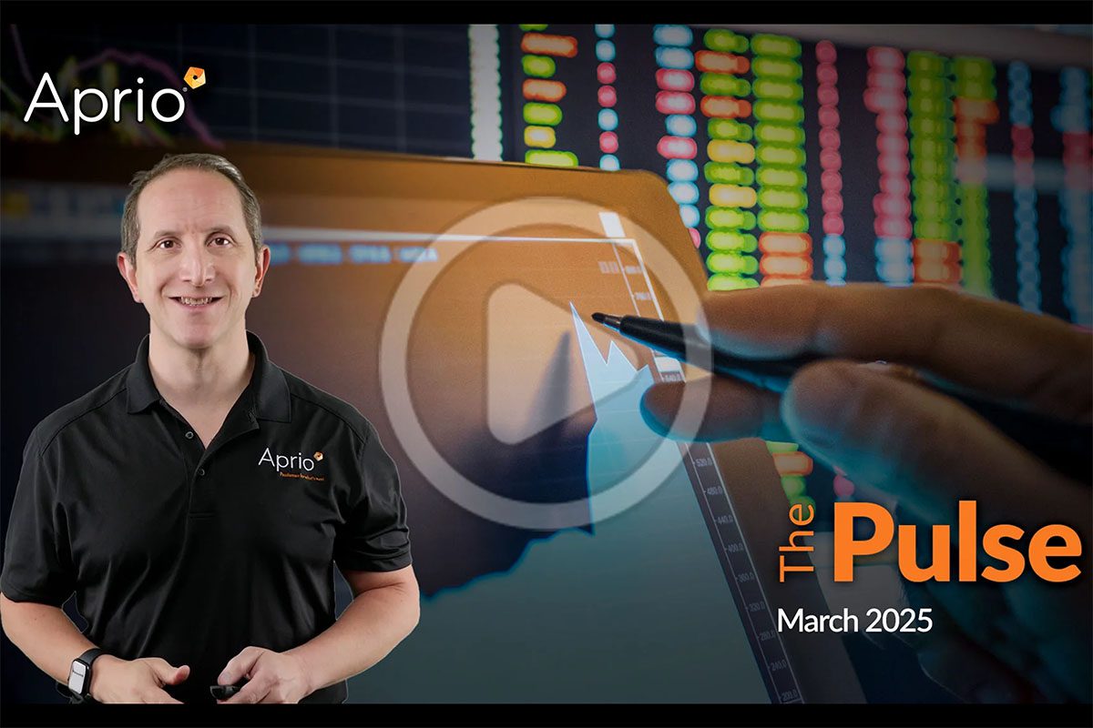 A man in an Aprio shirt stands next to a digital display showing charts and graphs, with The Pulse March 2025 and the Aprio logo visible.