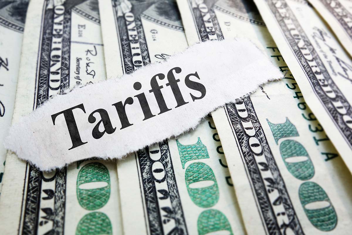 A torn piece of paper with the word Tariffs lies on top of spread out U.S. hundred-dollar bills.