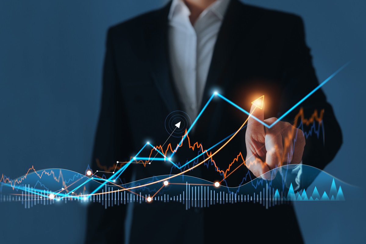 A person in a suit points at a glowing upward arrow on a digital financial chart with various line and bar graphs, symbolizing growth and data analysis.