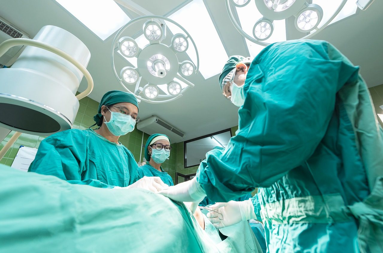 Three surgeons in green scrubs and masks perform an operation in a brightly lit operating room.