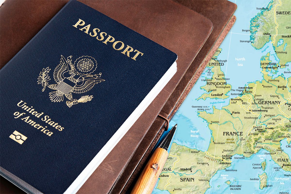 A United States passport, a pen, and a brown notebook placed next to a map of Europe showing countries like France, Germany, and the United Kingdom.