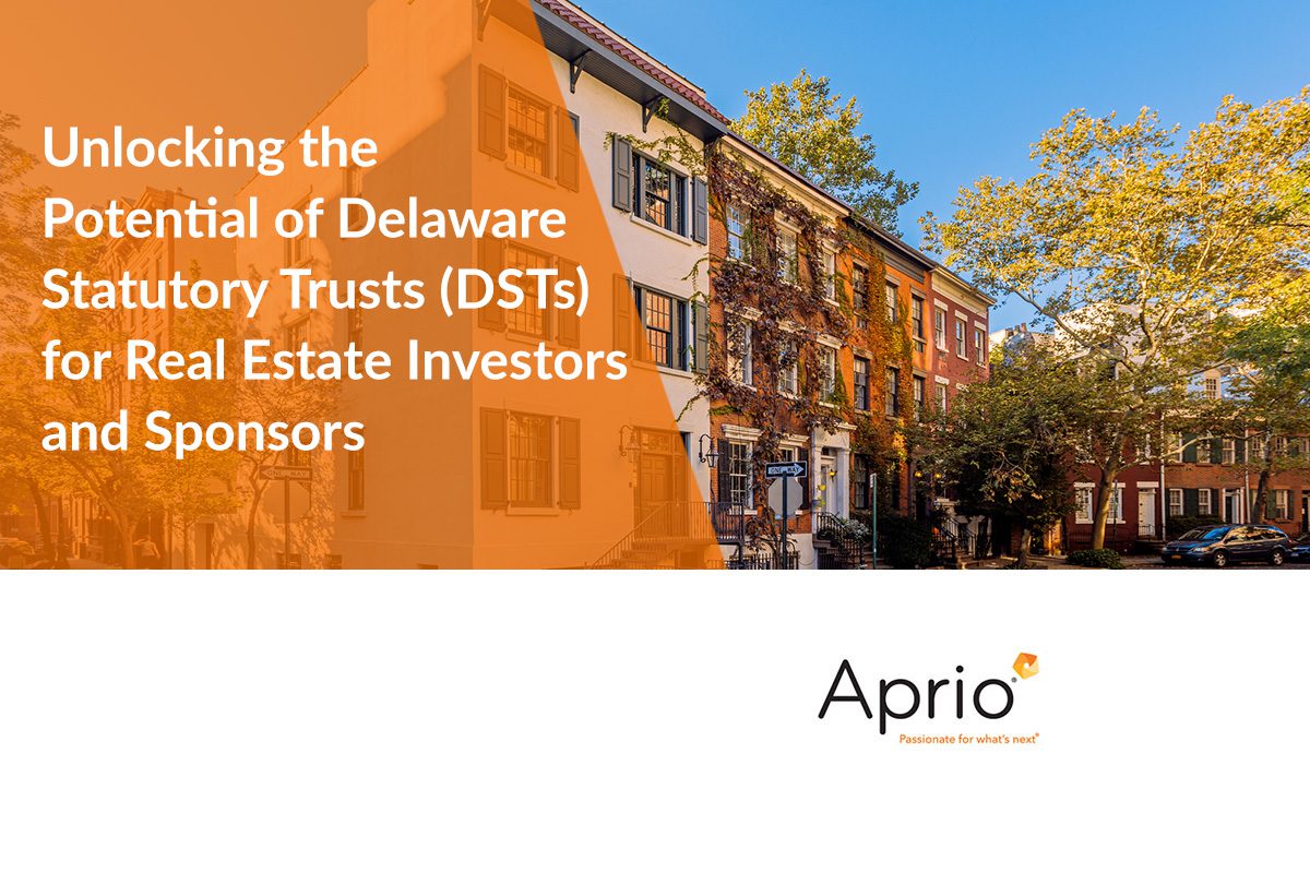 A row of brick townhouses with trees under a blue sky, overlaid with text about Delaware Statutory Trusts (DSTs) for real estate investors and sponsors, and the Aprio logo.