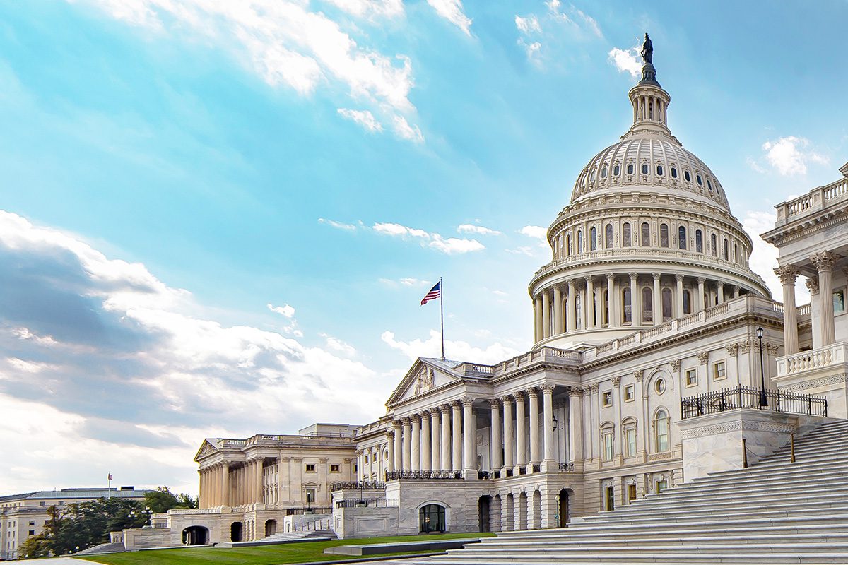 The United States Capitol building with a U.S. flag flying, seen from the west on a partly cloudy day.