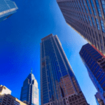 Tall skyscrapers seen from below against a clear blue sky in an urban cityscape.