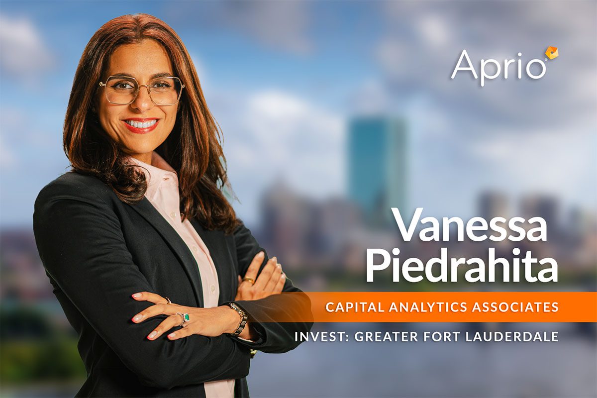 A woman with long brown hair and glasses stands smiling with arms crossed; text reads Vanessa Piedrahita, Capital Analytics Associates, Invest: Greater Fort Lauderdale, Aprio.