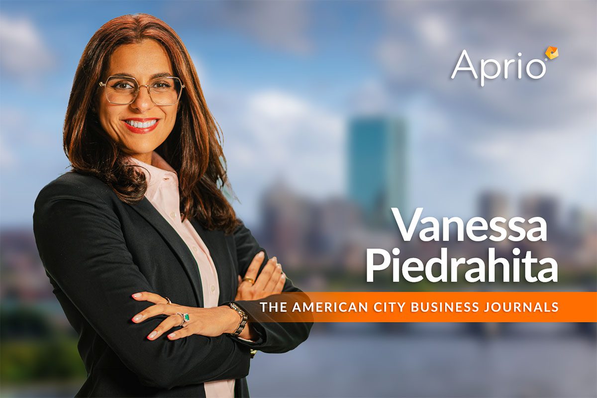 A woman with long brown hair and glasses stands with arms crossed, smiling, next to text reading Vanessa Piedrahita, The American City Business Journals and the Aprio logo.