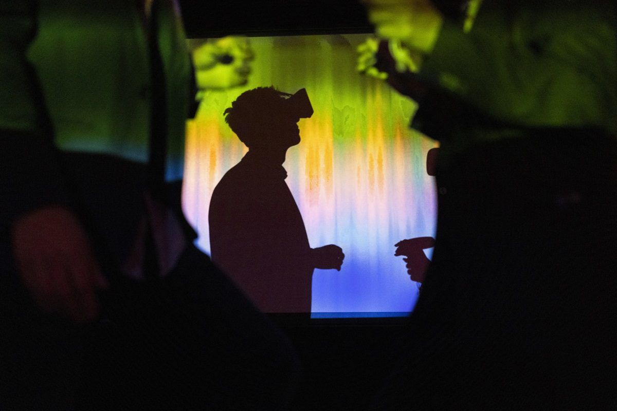 Silhouette of a person wearing a virtual reality headset, surrounded by abstract colorful light, with blurred figures in the foreground.