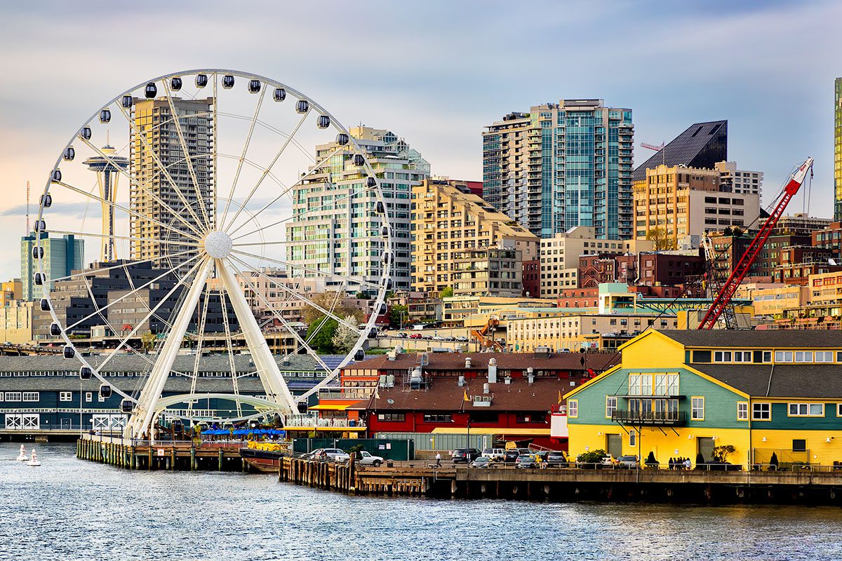A waterfront cityscape with a large Ferris wheel, colorful buildings, and modern high-rise structures in the background.