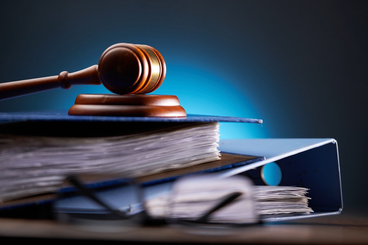 A judges gavel rests on a closed file folder, with stacked documents and a pair of eyeglasses in the foreground.
