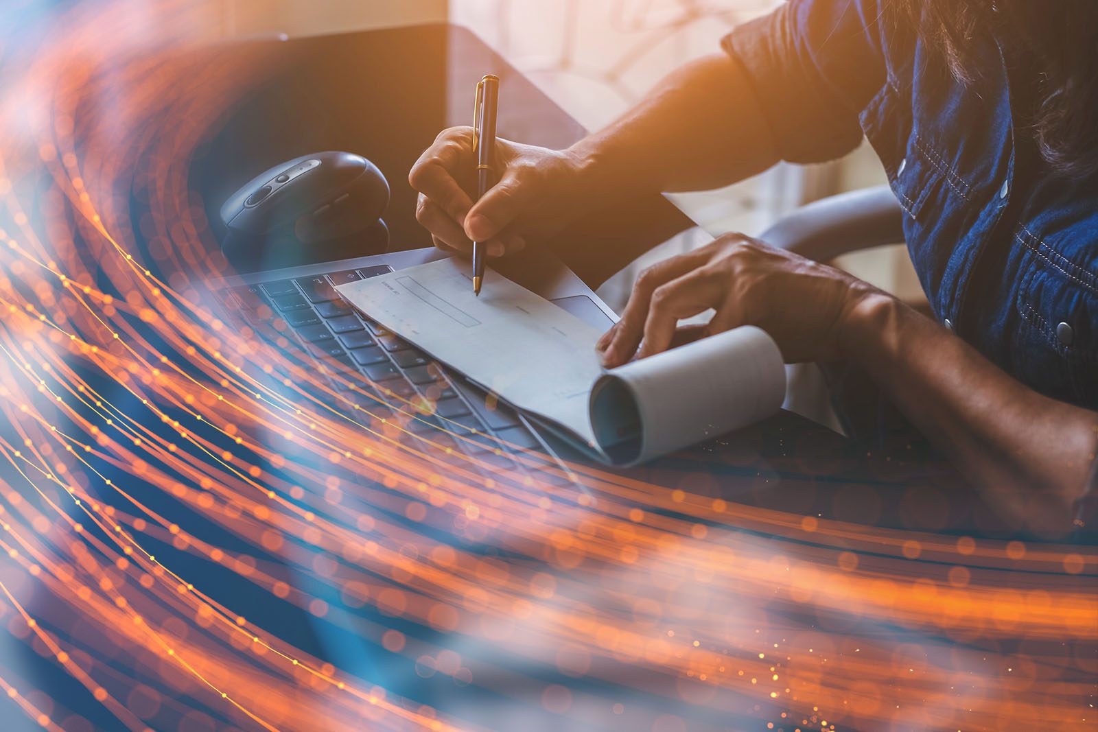 A person writes a check on a desk with a laptop and mouse, overlaid with orange light streaks suggesting digital or financial technology themes.