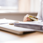 A person holding glasses sits at a desk with documents and a notebook, appearing to review paperwork.